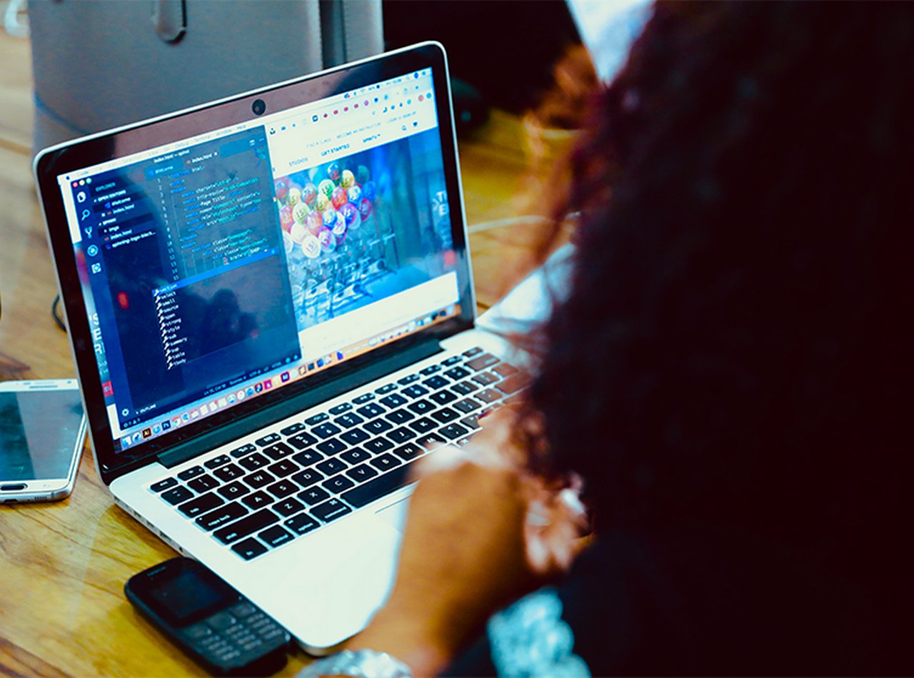 A woman from behind with her laptop open; code can be seen on the screen