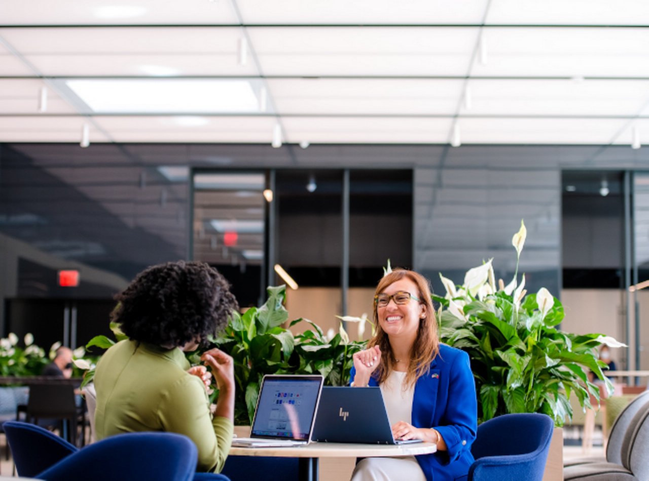 two women with laptop sitting at a table and laughing