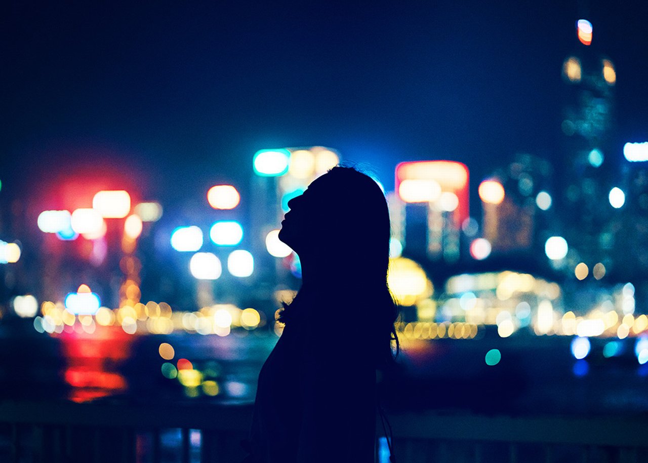 A woman's silhouette in front of the blurry lights of a city