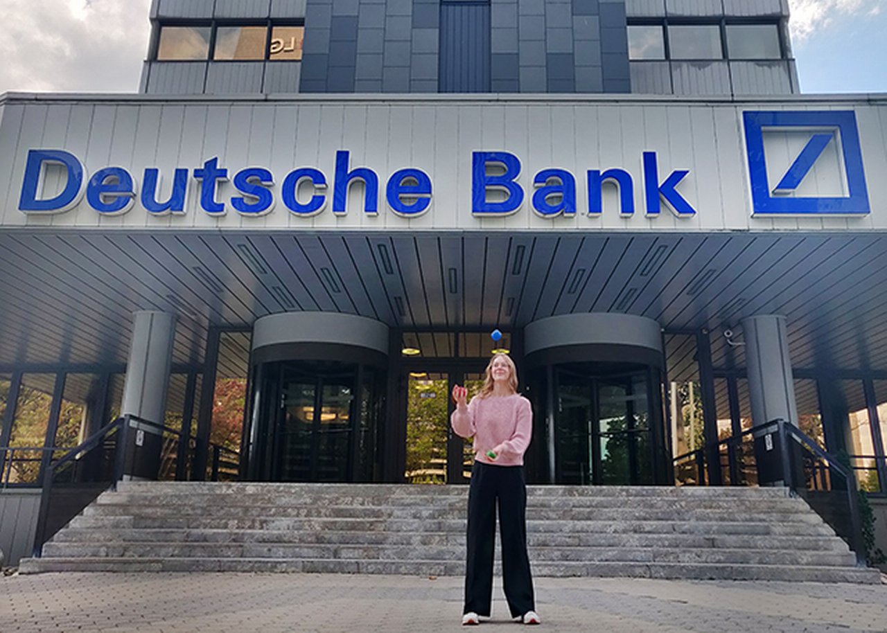 Nina jongliert vor einem Gebäude der Deutschen Bank